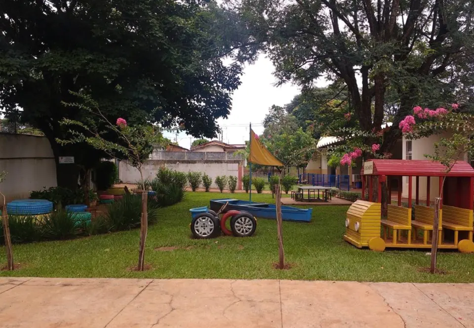 Área externa da creche com gramado, árvores e brinquedos de parque