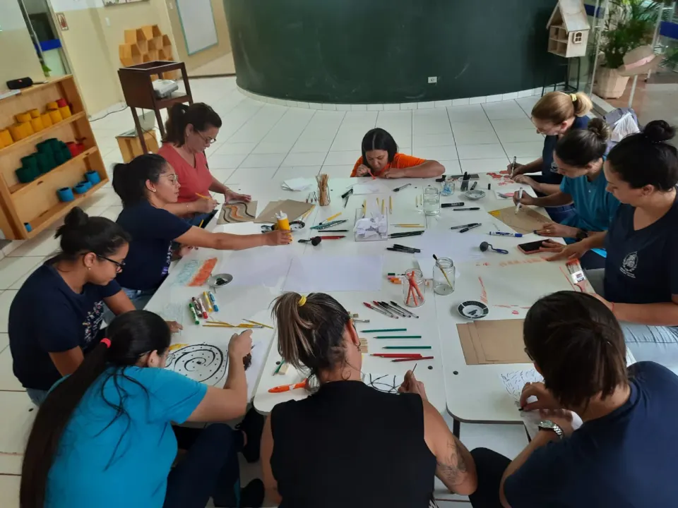 Educadoras reunidas em torno de uma grande mesa durante um encontro de formação