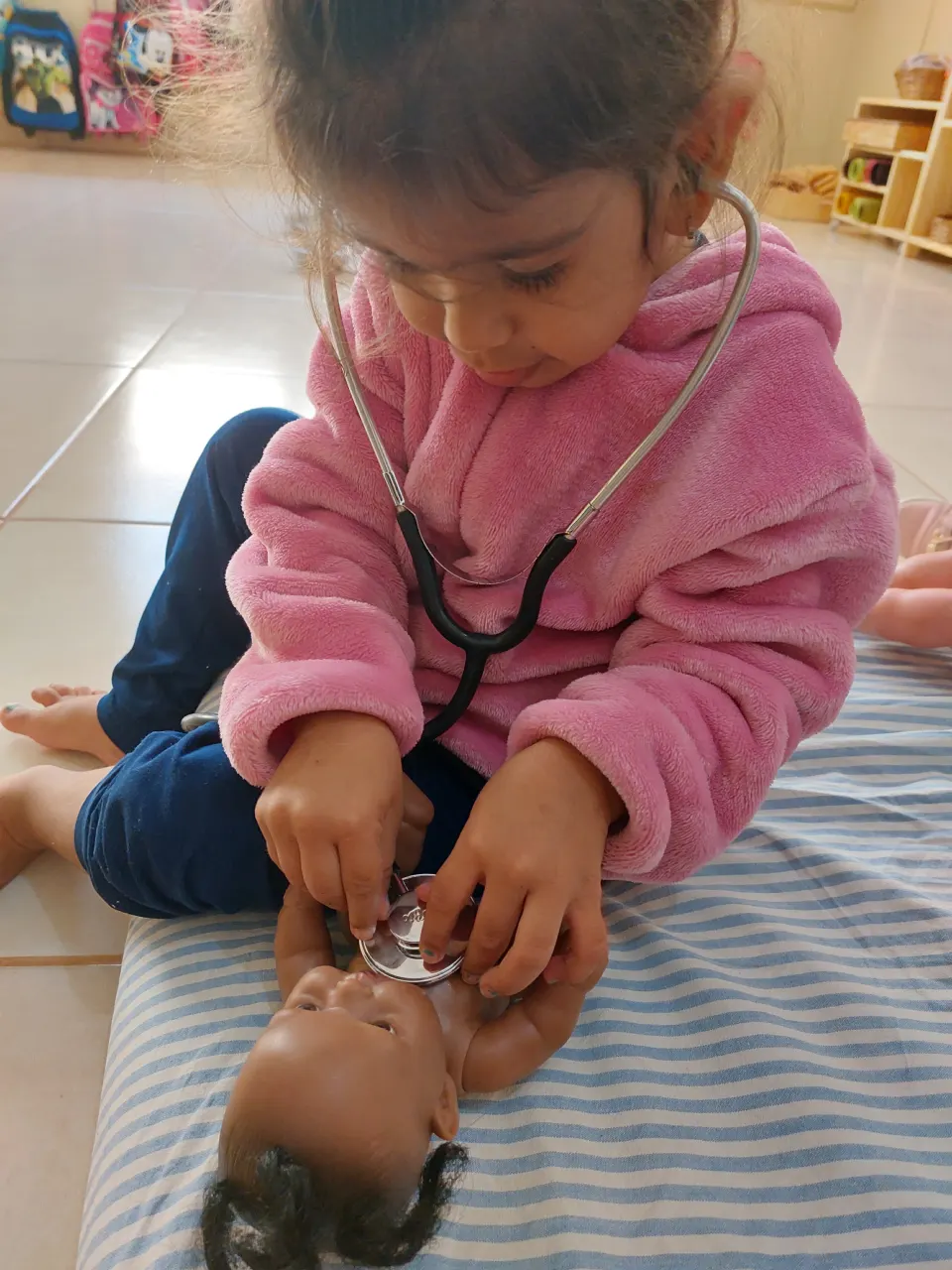 Criança brincando de médica com um estetoscópio e uma boneca