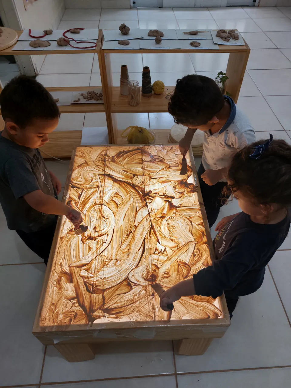 Crianças explorando com as mãos uma mesa de areia iluminada