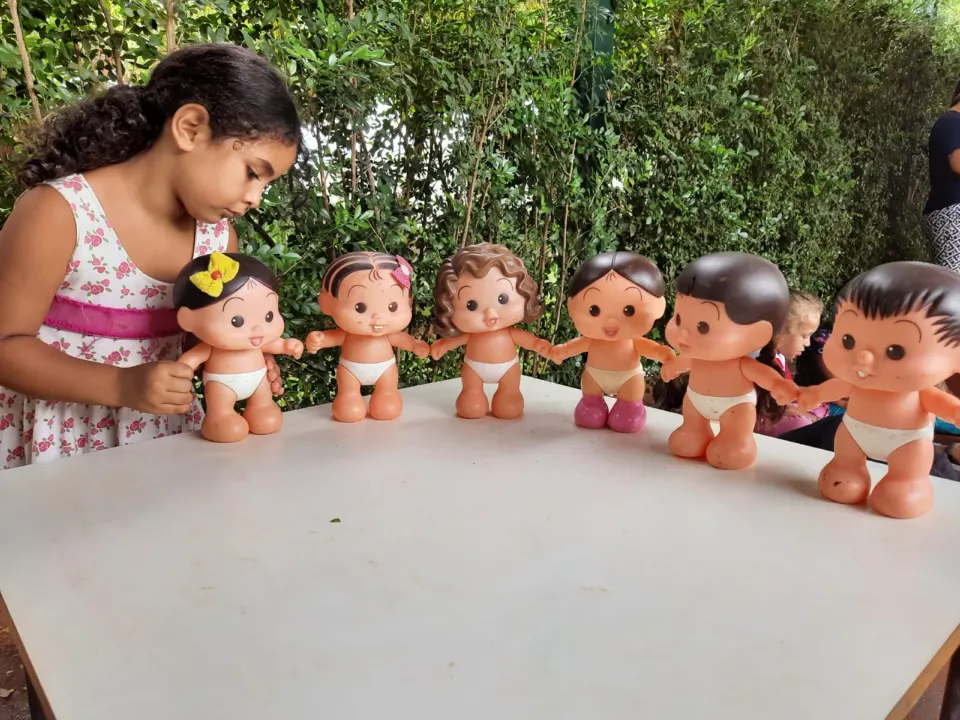 Menina organizando bonecos em fila sobre uma mesa no jardim