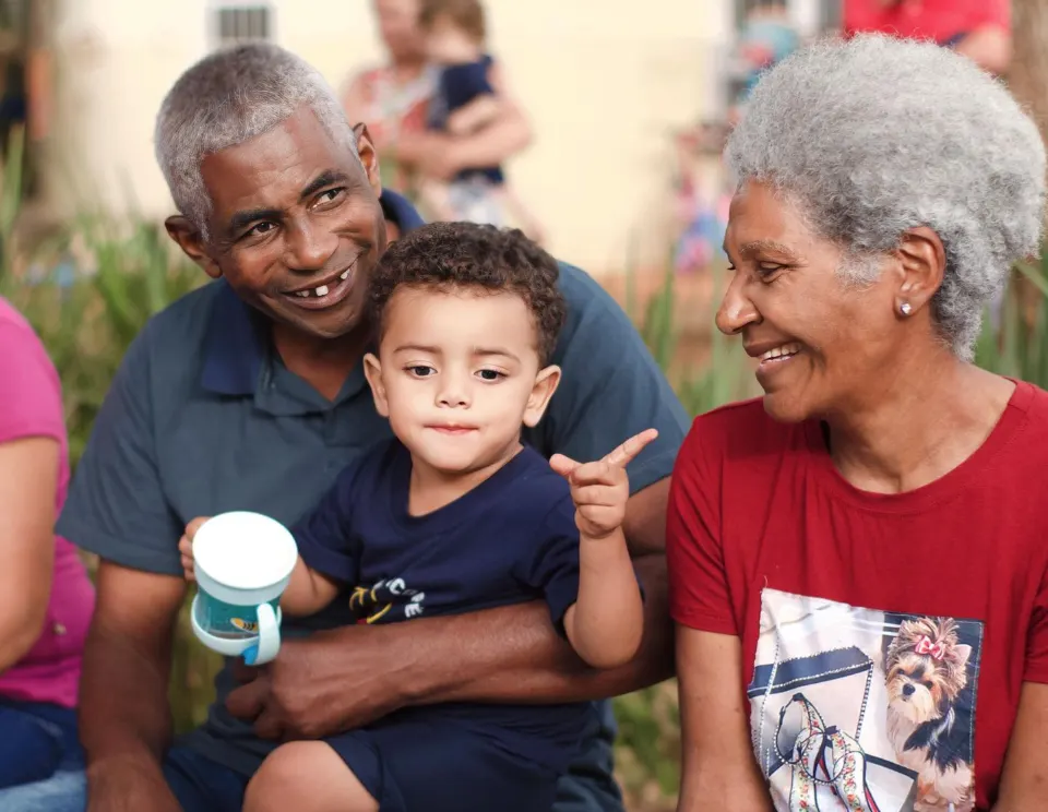 Criança sorrindo no colo, entre dois familiares, em um encontro na creche