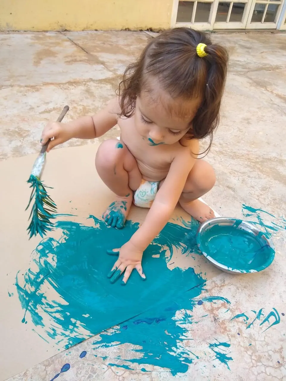 Criança pintando o chão com tinta azul e um pincel
