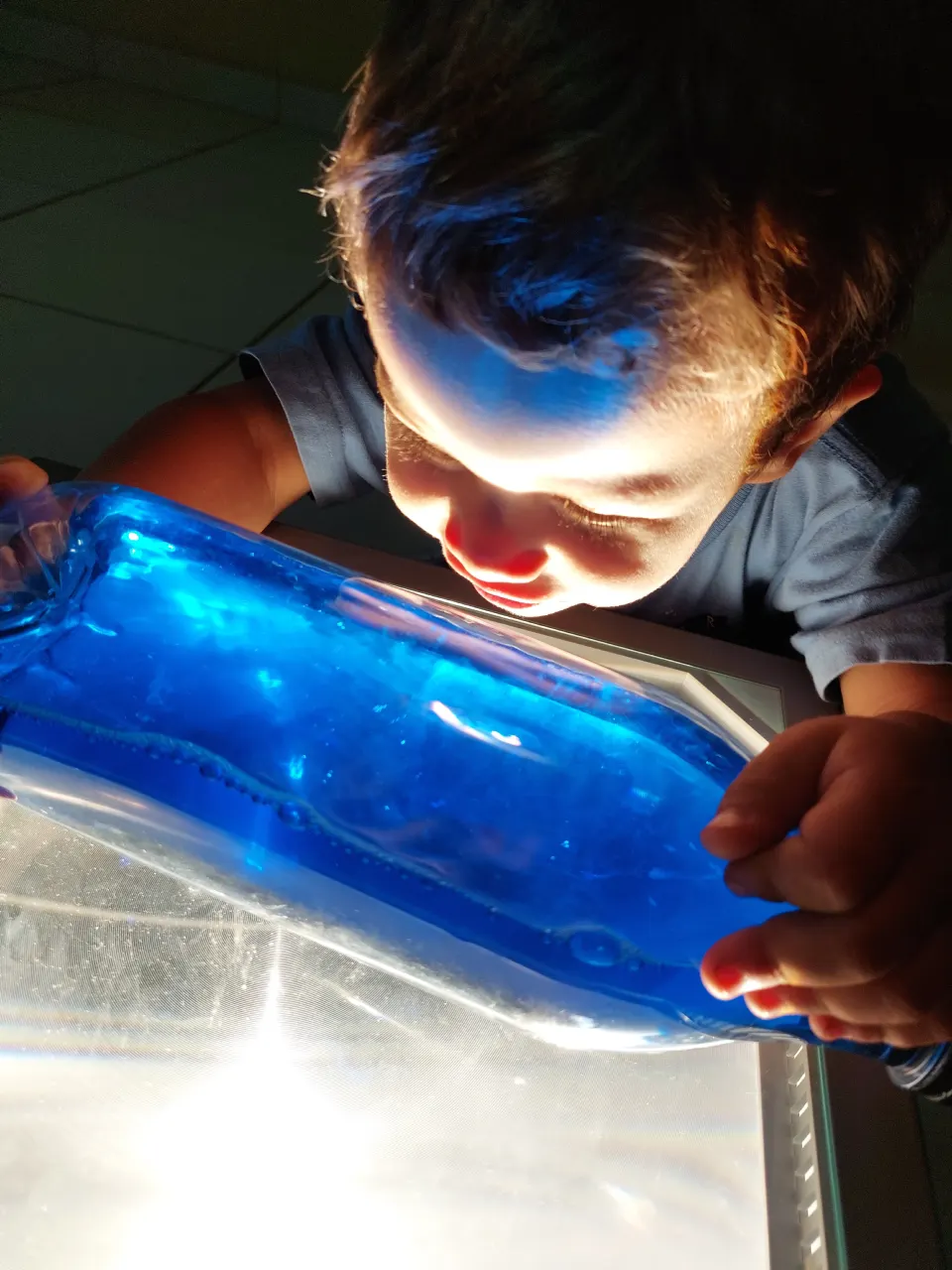 Criança iluminada pela luz azul de uma bolsa sensorial sobre a mesa de luz